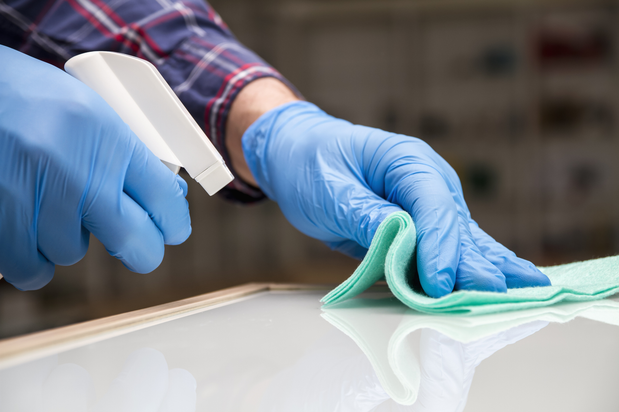 A man in blue protective gloves disinfects the surfaces of an audio and video equipment store using a rag and spray disinfectant. Protection from bacteria and viruses.